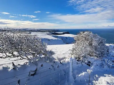 a fence covered in snow next to the ocean at Appleloft in Saint Gennys