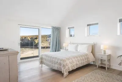 a white bedroom with a bed and a large window at Shore Edge in Portreath
