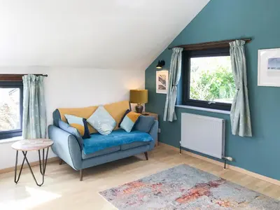 a living room with a blue couch and two windows at Little Fursdon Apartment in Liskeard