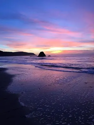 a sunset on a beach with a rock in the ocean at Swallows Nest at Widemouth Bay - 2 bedroom cottage in Bude