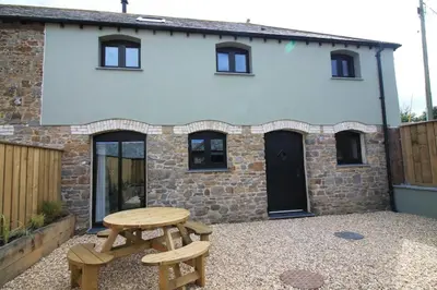 a table and two benches in front of a house at Swallows Nest at Widemouth Bay - 2 bedroom cottage in Bude