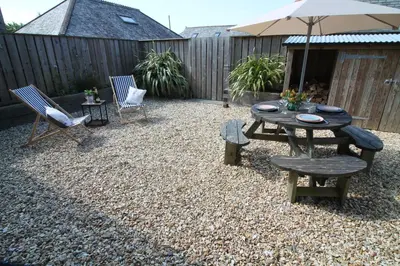 a patio with a table and chairs and an umbrella at The Stable at Widemouth Bay - 2 bedroom cottage in Poundstock