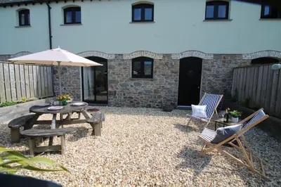a patio with a table and chairs and an umbrella at The Stable at Widemouth Bay - 2 bedroom cottage in Poundstock