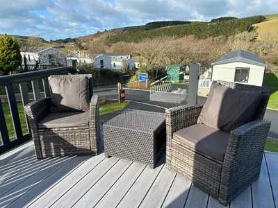 two wicker chairs and a table on a deck at Mawgan Pads Lazy Days Lodge in Mawgan Porth