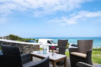 a table and chairs on a patio with the ocean at Bellevue, Port Isaac Bay Holidays in Port Isaac