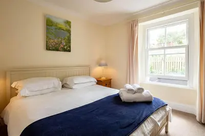 a bedroom with a bed with a blue blanket and a window at Bellevue, Port Isaac Bay Holidays in Port Isaac