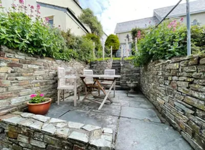 a patio with a table and chairs in a stone wall at Waypast, Port Isaac Bay Holidays in Port Isaac