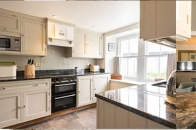 a kitchen with white cabinets and a black stove top oven at Kicker Cottage, Port Isaac Bay Holidays in Port Isaac