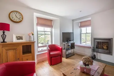 a living room with a red chair and a clock on the wall at Upper Deck, Port Isaac Bay Holidays in Port Isaac