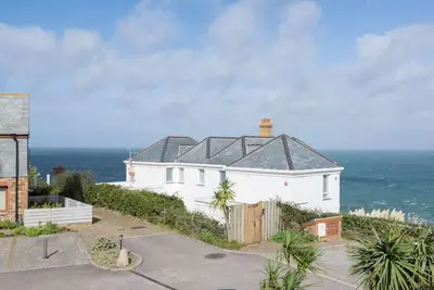 a white house with a black roof next to the ocean at Sea Gem, Port Isaac Bay Holidays in Port Isaac