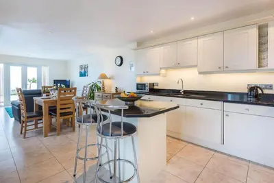 a kitchen with white cabinets and a table with bar stools at Sea Gem, Port Isaac Bay Holidays in Port Isaac