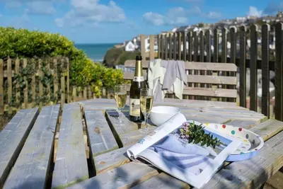 a wooden table with a bottle of wine and glasses at Scuppers, Port Isaac Bay Holidays in Port Isaac