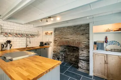 a kitchen with a stone fireplace and a counter at Windlass, Port Isaac Bay Holidays in Port Isaac