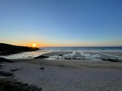 a beach with the sun setting on the ocean at The Little Snug in St Ives in St Ives