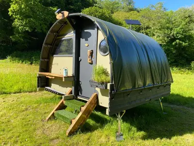 a trailer with awning and stairs in a field at Exclusive Use Riverside Landpods at Wildish Cornwall in Bodmin