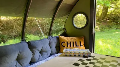 a couch in the back of a tent with a window at Exclusive Use Riverside Landpods at Wildish Cornwall in Bodmin