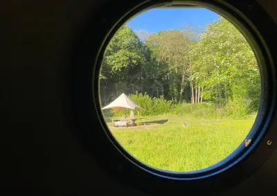 a round window view of a field with a tent at Exclusive Use Riverside Landpods at Wildish Cornwall in Bodmin