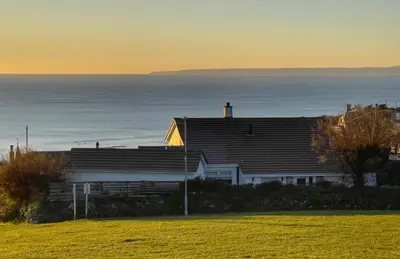 a house on a hill with the ocean in the background at Sunset Beach House Porthleven in Porthleven