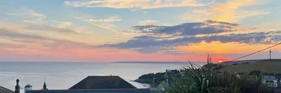 a sunset over a body of water with buildings and the ocean at Sunset Beach House Porthleven in Porthleven