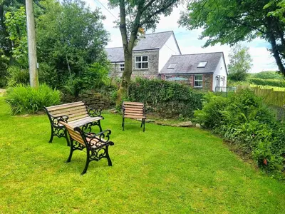 two benches sitting in the grass in front of a house at The Old Farmhouse in Michaelstow