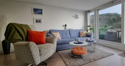 a living room with a blue couch and a window at May View - Luxury Sea View Apartment - Millendreath, Looe in Looe