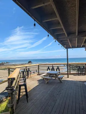 a wooden deck with picnic tables and chairs on the beach at May View - Luxury Sea View Apartment - Millendreath, Looe in Looe