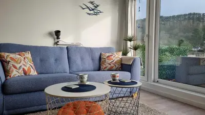 a living room with a blue couch and two tables at May View - Luxury Sea View Apartment - Millendreath, Looe in Looe