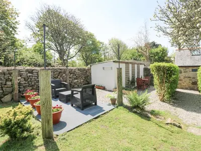 a garden with a stone wall and a patio at Godolphin Barn in Helston