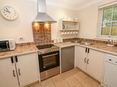 a kitchen with white cabinets and a clock on the wall at Tregonning Lodge in Helston