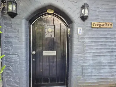 a black door in a blue brick building with lights at Tregarthen Cottage - tranquil self-contained room near Looe offering easy parking right outside with EV point in Looe