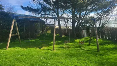 a playground with two swings in a field of grass at Honeycomb Lodge - Holiday Home 5 min from Padstow in Padstow