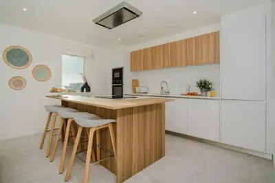 a kitchen with white cabinets and a wooden island with stools at 7 Cliff Edge in Newquay