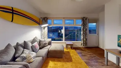 a living room with a couch and a surfboard on the wall at A18 Bojago, Riviere Towans in Hayle