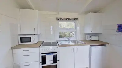 a kitchen with white cabinets and a sink and a microwave at B14 Amulree, Riviere Towans in Hayle