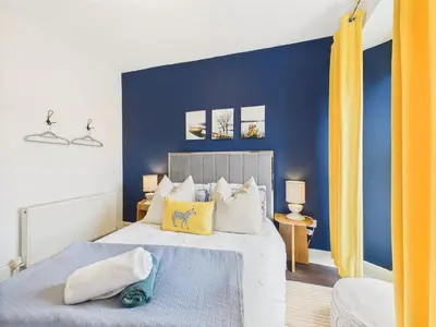 a bedroom with blue walls and a bed with yellow curtains at Central Falmouth Flat with Free Parking in Falmouth