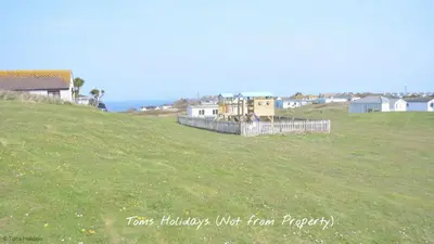 a field of green grass with houses and the ocean at B44 Sea Urchin, Riviere Towans in Hayle