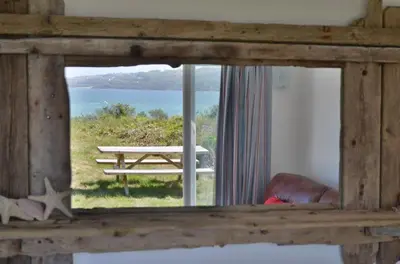 a view of a picnic table and the ocean through a window at B45 Phillippa, Riviere Towans in Hayle