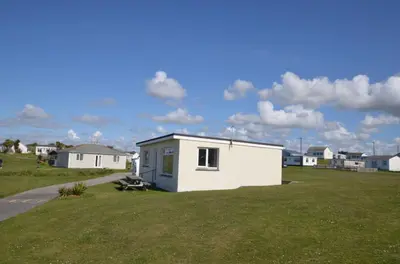 a small white building on a grass field at B50 Kingfisher, Riviere Towans in Hayle