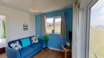 a blue living room with a blue couch and a window at B50 Kingfisher, Riviere Towans in Hayle