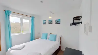 a bedroom with a bed with blue pillows and a window at B52 Oyster, Riviere Towans in Hayle