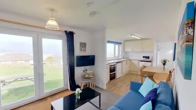 a living room with a blue couch and a kitchen at B52 Oyster, Riviere Towans in Hayle