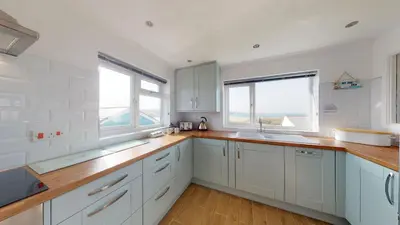 a kitchen with white cabinets and two windows at C20 Y Worry, Riviere Towans in Hayle