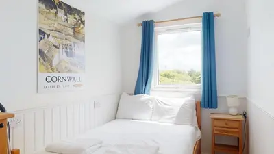 a bedroom with a bed and a window with blue curtains at C25 Weir View, Riviere Towans in Hayle