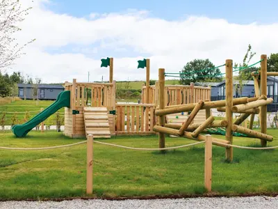 a playground with wooden play equipment in a park at Penmarlam Lodge Retreat 12 in Fowey