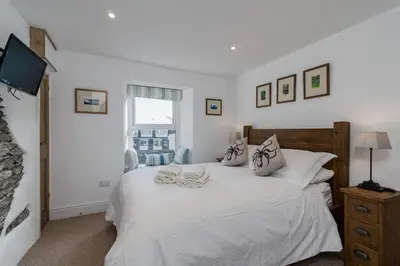 a bedroom with a white bed and a window at Jessamine: Restored fisherman's cottage close to Looe's harbour in Looe