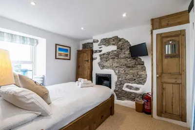 a bedroom with a bed and a stone fireplace at Jessamine: Restored fisherman's cottage close to Looe's harbour in Looe