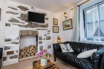 a living room with a black leather couch and a fireplace at Jessamine: Restored fisherman's cottage close to Looe's harbour in Looe