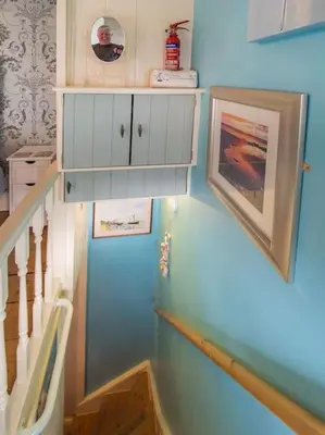 a stairway with a blue wall with a white cabinet at Birds Nest Cottage Looe in Looe