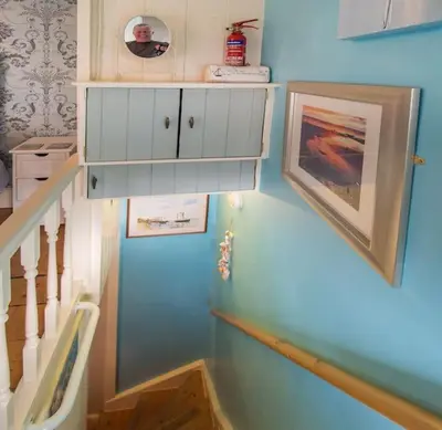a stairway with a blue wall with a white cabinet at Birds Nest Cottage Looe in Looe