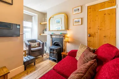 a living room with a red couch and a fireplace at Birds Nest Cottage Looe in Looe